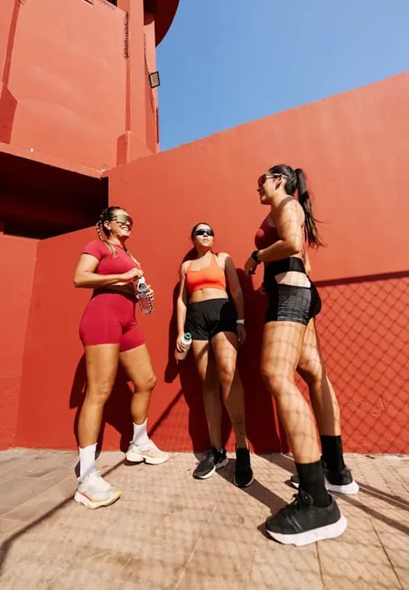 Three women in athletic wear against a red wall